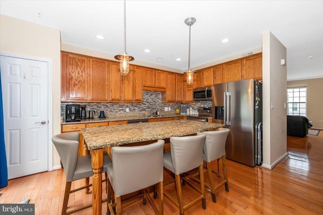 kitchen featuring appliances with stainless steel finishes, light wood finished floors, tasteful backsplash, brown cabinetry, and recessed lighting