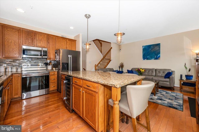 kitchen featuring appliances with stainless steel finishes, beverage cooler, a breakfast bar, light stone countertops, and light wood-style flooring