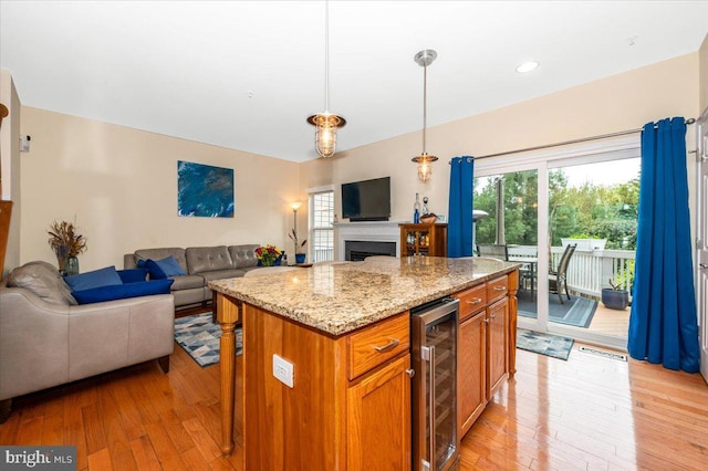 kitchen with beverage cooler, open floor plan, light wood-style floors, light stone counters, and hanging light fixtures