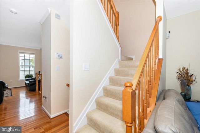 stairs featuring wood finished floors, baseboards, and crown molding