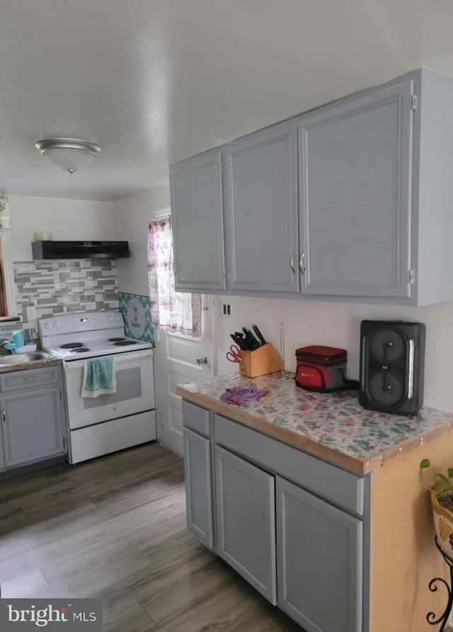 kitchen featuring decorative backsplash, light countertops, gray cabinets, under cabinet range hood, and electric stove