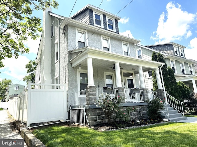 american foursquare style home featuring ceiling fan, stucco siding, a front yard, a chimney, and covered porch