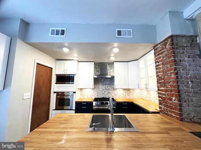 2117 Kearny St NE, Washington, DC 20018 - kitchen featuring butcher block counters, stainless steel appliances, wall chimney range hood, a sink, and white cabinets