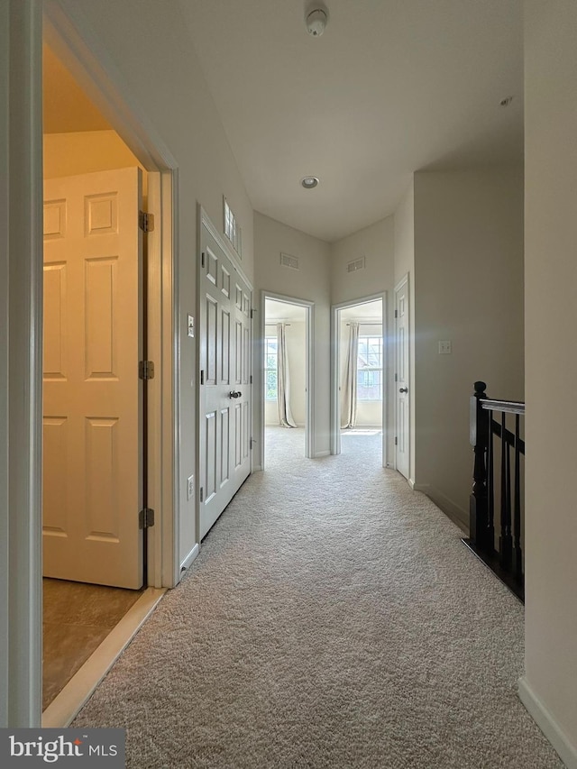 corridor with carpet flooring, baseboards, and an upstairs landing