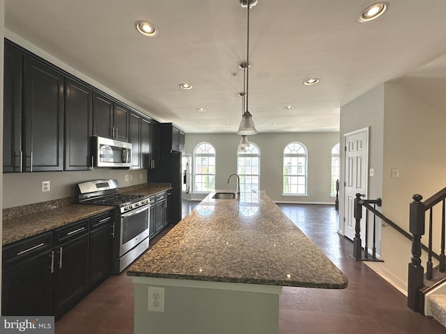 kitchen featuring appliances with stainless steel finishes, a sink, dark cabinetry, recessed lighting, and a center island with sink