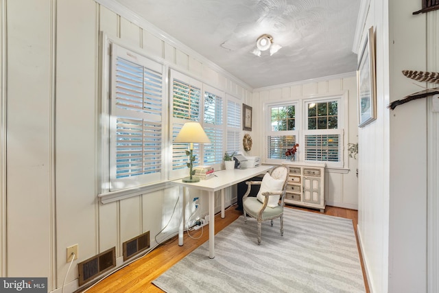 office featuring light wood finished floors, crown molding, visible vents, and a decorative wall