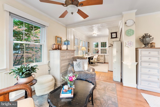 sitting room with light wood finished floors, a wainscoted wall, a ceiling fan, and ornamental molding
