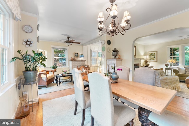 dining space featuring crown molding, light wood-type flooring, ceiling fan with notable chandelier, and arched walkways