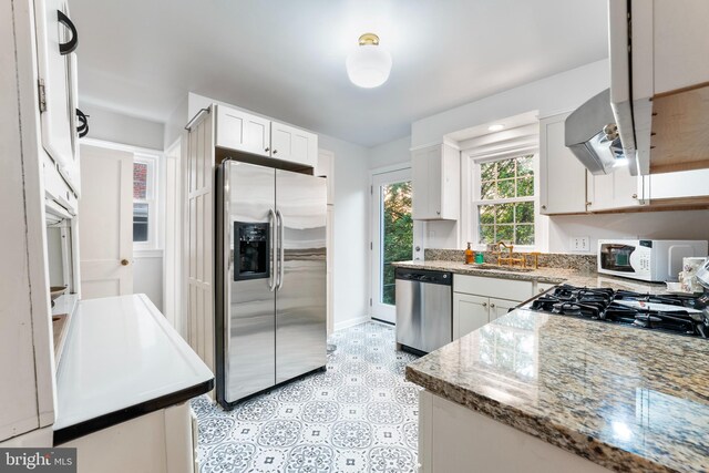 kitchen with a sink, stainless steel appliances, ventilation hood, white cabinets, and baseboards