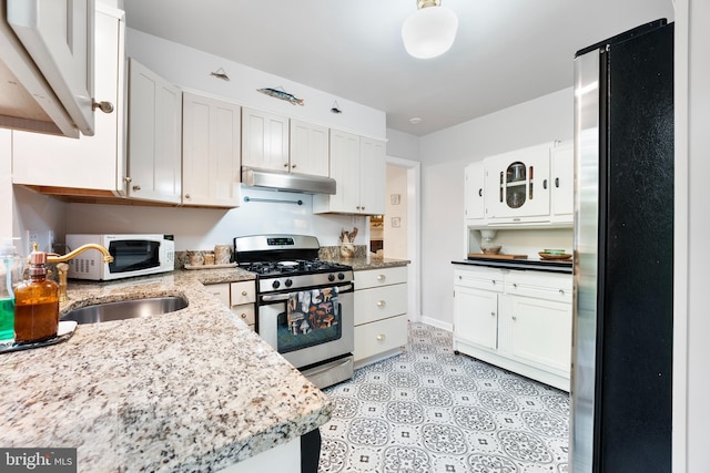 kitchen featuring light floors, under cabinet range hood, white cabinets, light stone countertops, and appliances with stainless steel finishes