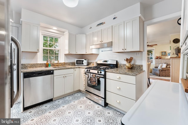 kitchen with a ceiling fan, under cabinet range hood, a sink, white cabinets, and appliances with stainless steel finishes