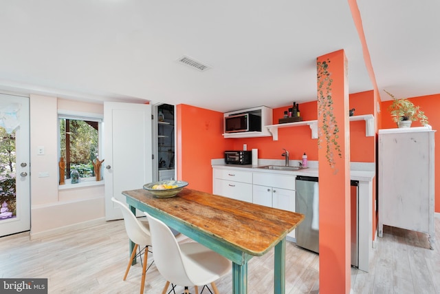 kitchen with a sink, light wood-style flooring, visible vents, and white cabinets