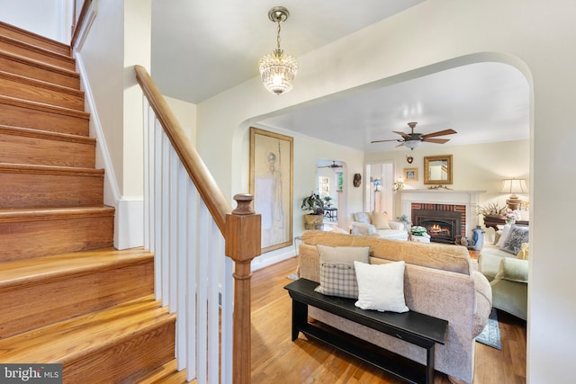 living area featuring a fireplace, stairs, arched walkways, and wood finished floors