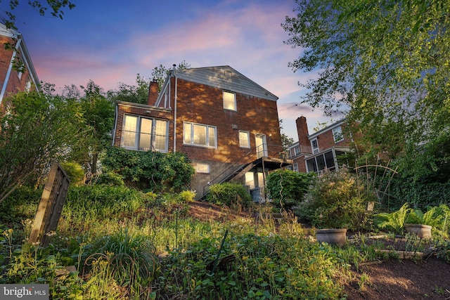 back of house at dusk featuring brick siding, stairway, and a chimney
