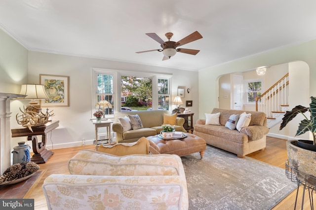 living area with wood finished floors, stairway, crown molding, ceiling fan, and arched walkways