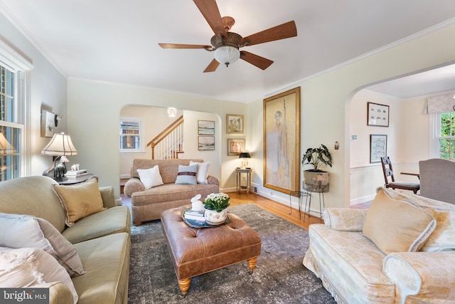 living room with ceiling fan, crown molding, stairway, and arched walkways
