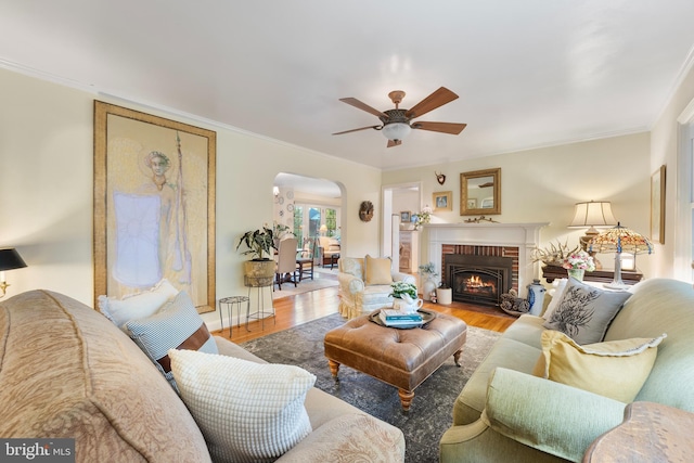 living area with a ceiling fan, crown molding, wood finished floors, arched walkways, and a fireplace