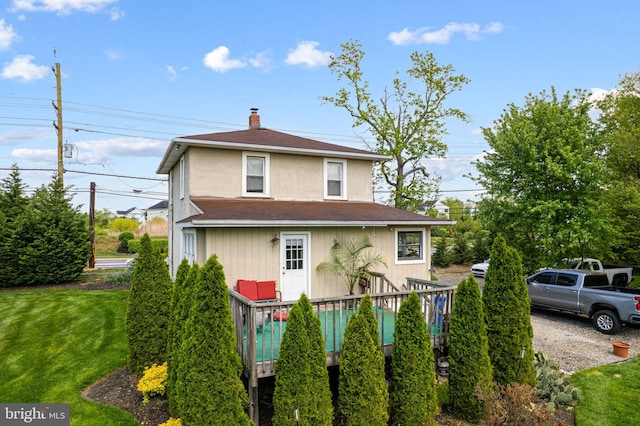 view of front of house featuring stucco siding, a chimney, a deck, a front yard, and roof with shingles