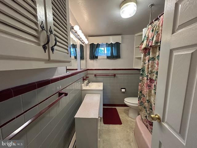 bathroom featuring vanity, toilet, a wainscoted wall, tile walls, and curtained shower