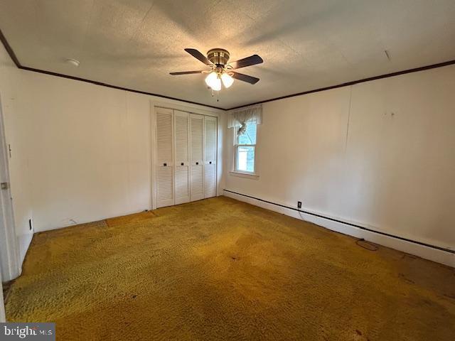 unfurnished bedroom with ceiling fan, crown molding, a baseboard radiator, a closet, and carpet