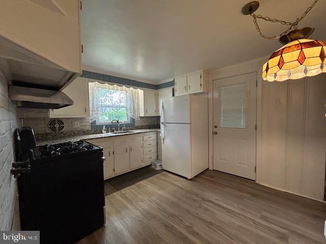 kitchen with black gas range, freestanding refrigerator, dark wood-style floors, under cabinet range hood, and a sink