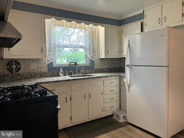 kitchen featuring freestanding refrigerator, ornamental molding, black gas stove, wall chimney exhaust hood, and a sink