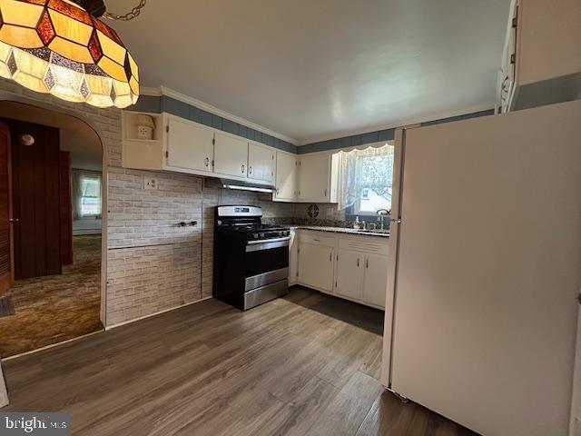 kitchen featuring stainless steel range with gas stovetop, arched walkways, freestanding refrigerator, white cabinetry, and dark wood-type flooring