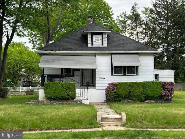 bungalow featuring roof with shingles, a chimney, and a front lawn