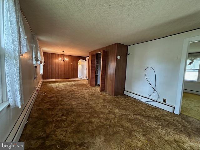 corridor featuring arched walkways, wood walls, carpet, and a baseboard radiator