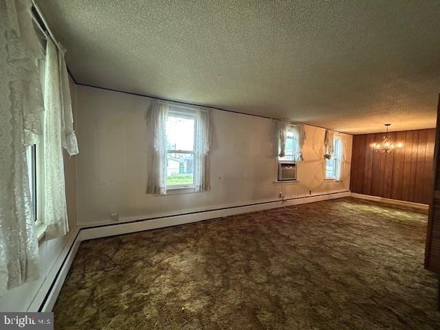 empty room featuring an inviting chandelier, dark carpet, a textured ceiling, and a healthy amount of sunlight