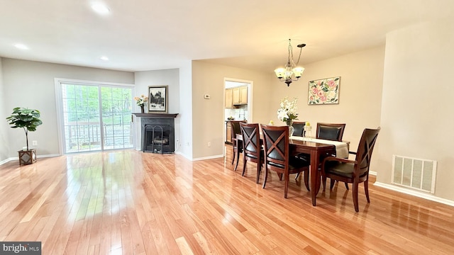 dining space with an inviting chandelier, a fireplace, light wood-style flooring, baseboards, and visible vents