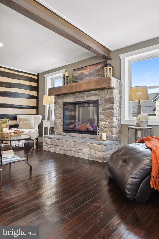 living area with beamed ceiling, a stone fireplace, hardwood / wood-style flooring, and plenty of natural light