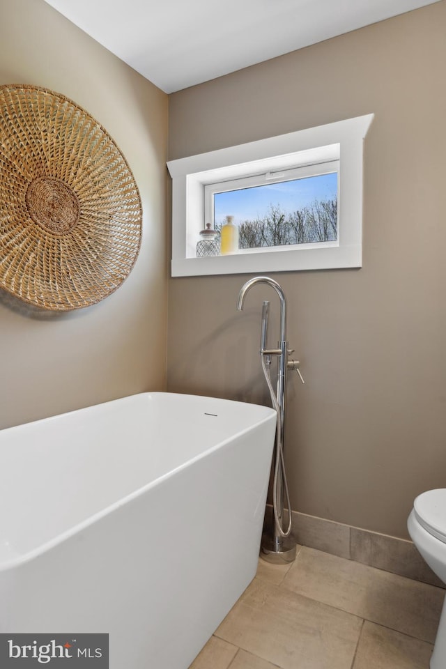 bathroom with a freestanding tub, toilet, and tile patterned floors