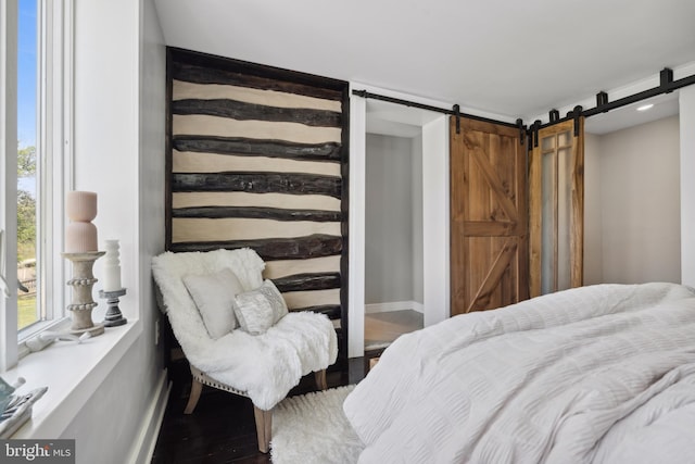 bedroom with baseboards, a barn door, and wood finished floors