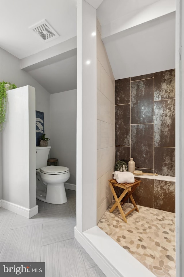 bathroom featuring visible vents, a tile shower, vaulted ceiling, and toilet