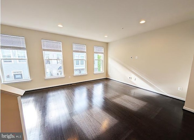empty room featuring recessed lighting, baseboards, and dark wood-type flooring