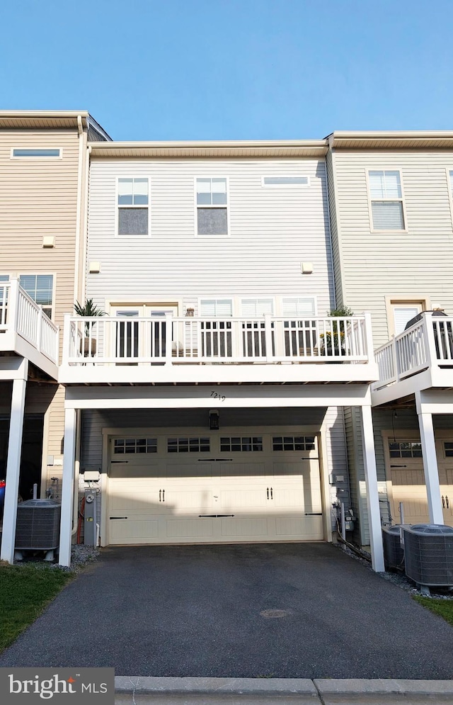 rear view of property featuring driveway, central AC unit, and a garage