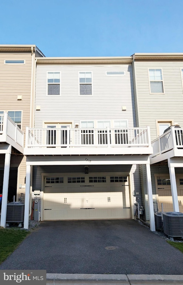 rear view of property with an attached garage, cooling unit, and aphalt driveway