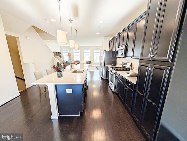 kitchen with dark wood-type flooring, a sink, a center island with sink, and stainless steel appliances