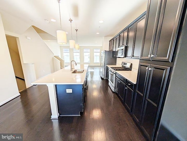 kitchen featuring appliances with stainless steel finishes, a sink, light countertops, dark wood-type flooring, and a center island with sink