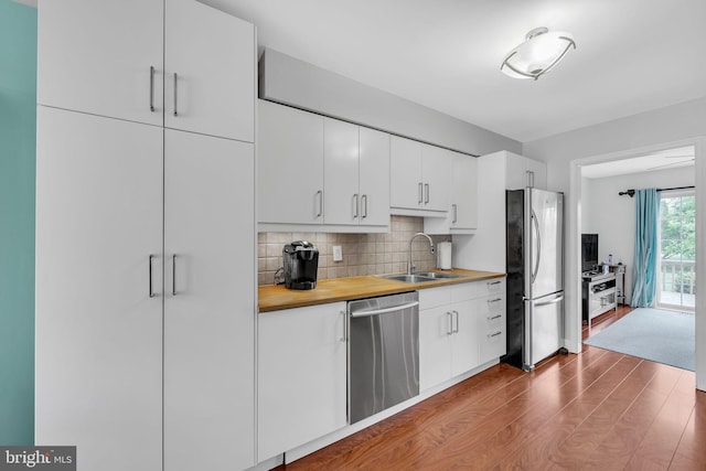 kitchen featuring appliances with stainless steel finishes, a sink, wood finished floors, decorative backsplash, and white cabinetry