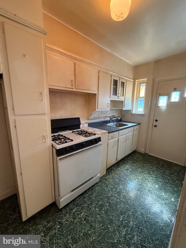 kitchen featuring white cabinets, white gas range oven, a sink, and tasteful backsplash