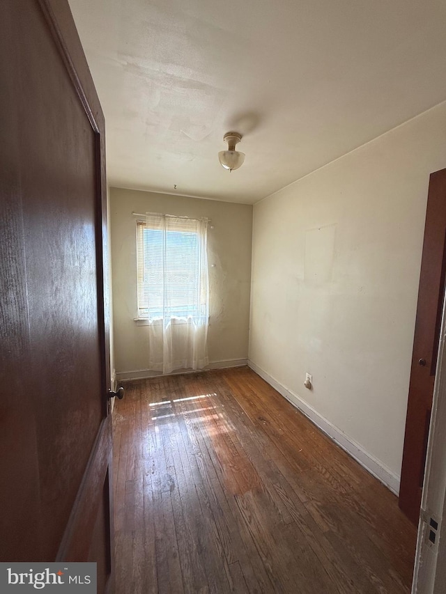 unfurnished room with baseboards and dark wood-type flooring
