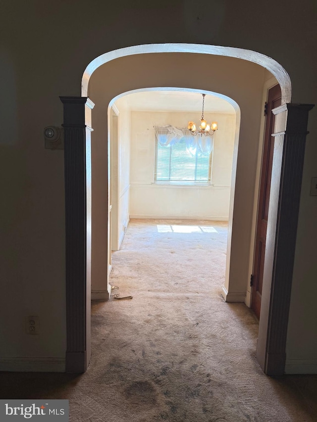 hallway featuring arched walkways, baseboards, carpet flooring, and a notable chandelier