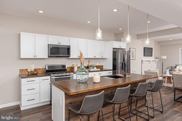 kitchen featuring dark wood-style flooring, appliances with stainless steel finishes, a center island with sink, a sink, and butcher block countertops