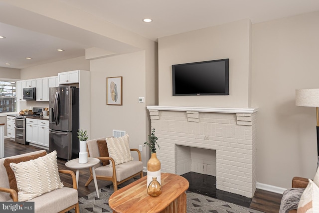 living area featuring visible vents, a brick fireplace, baseboards, dark wood-style floors, and recessed lighting