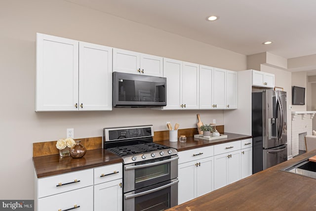 kitchen with appliances with stainless steel finishes, butcher block countertops, white cabinetry, recessed lighting, and backsplash