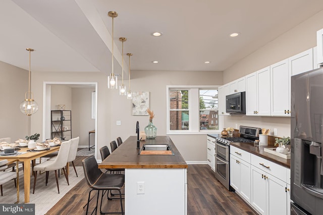 kitchen with appliances with stainless steel finishes, a sink, dark wood-style floors, a breakfast bar, and white cabinetry