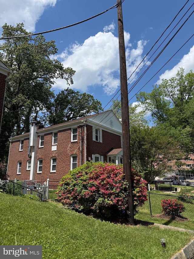 view of property exterior featuring a lawn, brick siding, and fence