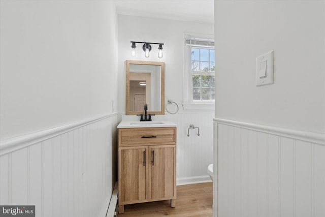 half bath with vanity, wainscoting, wood finished floors, and toilet